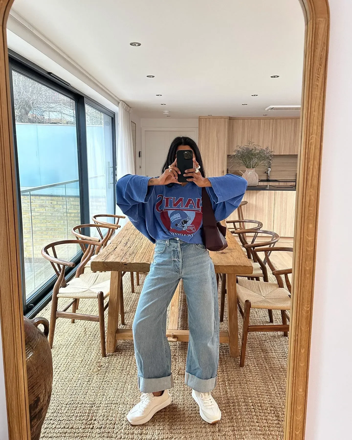 Look com tênis branco combina camiseta azul oversized com estampa vermelha, jeans claro de barra dobrada e bolsa marrom