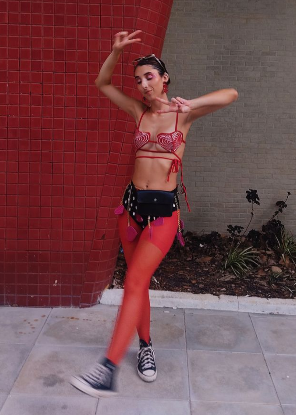 Modelo dança com top vermelho de coração em crochê, meia-calça vermelha e tênis preto estilo clássico, celebrando o Carnaval.