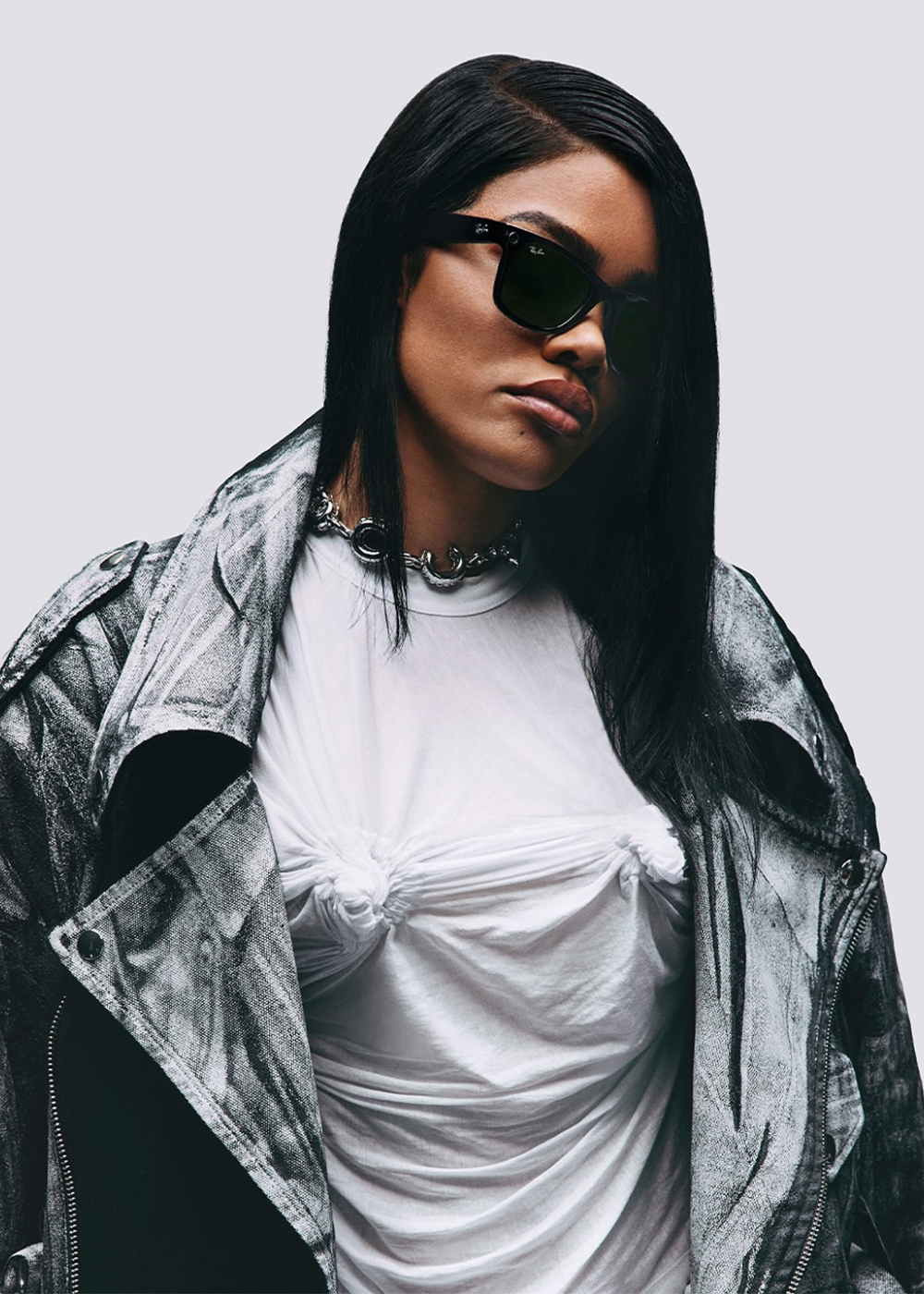 Modelo usa jaqueta oversized prateada com textura metálica, camiseta branca com nós frontais e colar chunky prata.