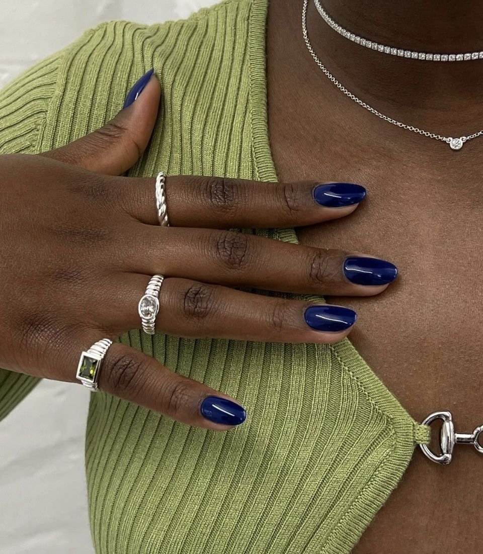 Mãos com unhas coloridas da moda em azul vibrante combinam com blusa canelada verde e joias prateadas delicadas.