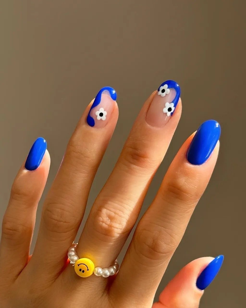 Unhas coloridas da moda em azul vibrante com acabamento brilhoso destacam mão adornada por anéis prateados e blusa verde