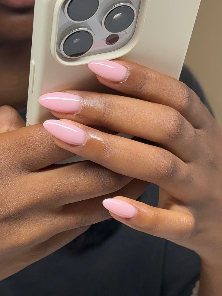 Unhas coloridas da moda em tom rosa claro com acabamento brilhante realçam mãos delicadas segurando celular bege,