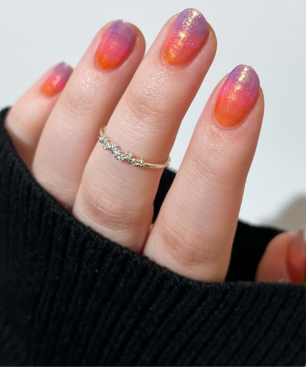 Unhas para o Carnaval com degrade em tons vibrantes de laranja, rosa e roxo, acabamento fosco com brilho dourado.