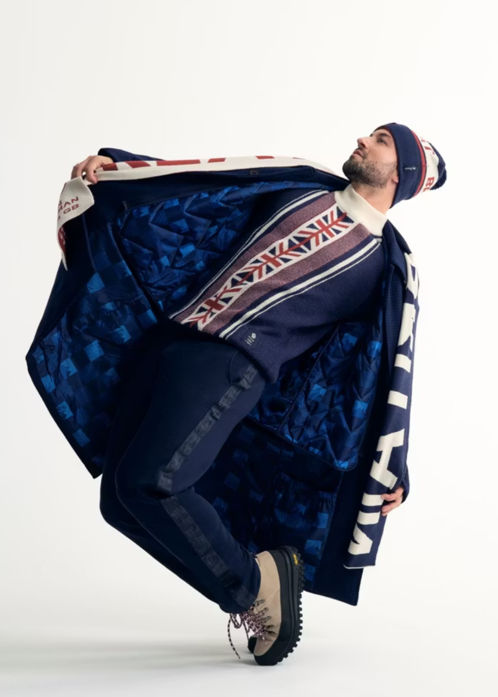 Homem inclina corpo para trás exibindo casaco azul com forro geométrico, suéter com estampa da bandeira britânica e gorro.
