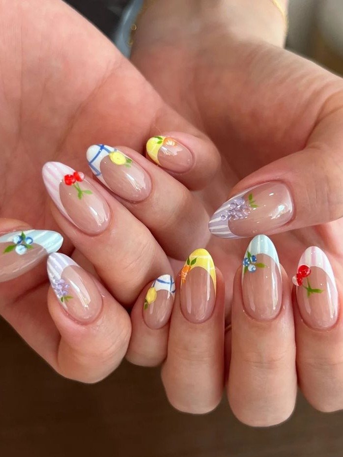 Unhas de verão com formato oval, base nude e pontas coloridas em listras suaves com delicadas frutas vermelhas, limão, uva
