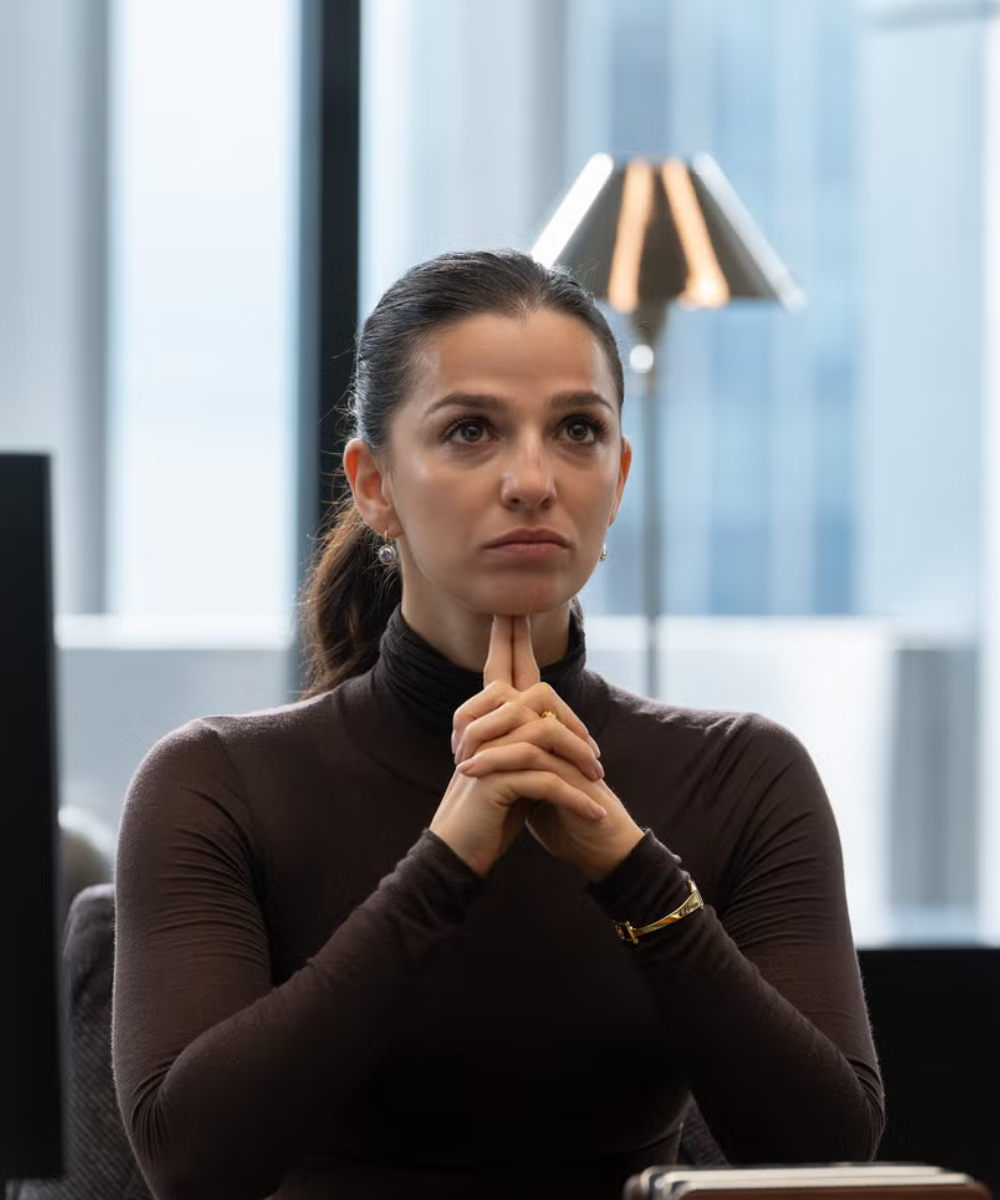 Mulher com blusa gola alta marrom justa em tecido leve, postura pensativa e tensa, clima sóbrio na quarta temporada de