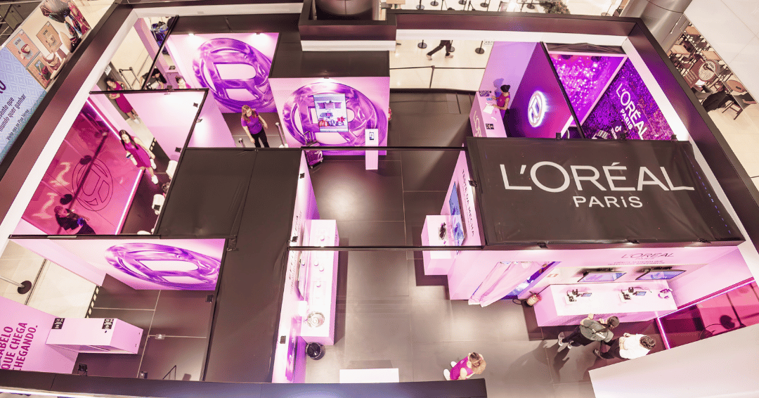 Futuro da beleza em estande rosa e preto da L'Oréal Paris com luz neon, telas imersivas e clima tecnológico.