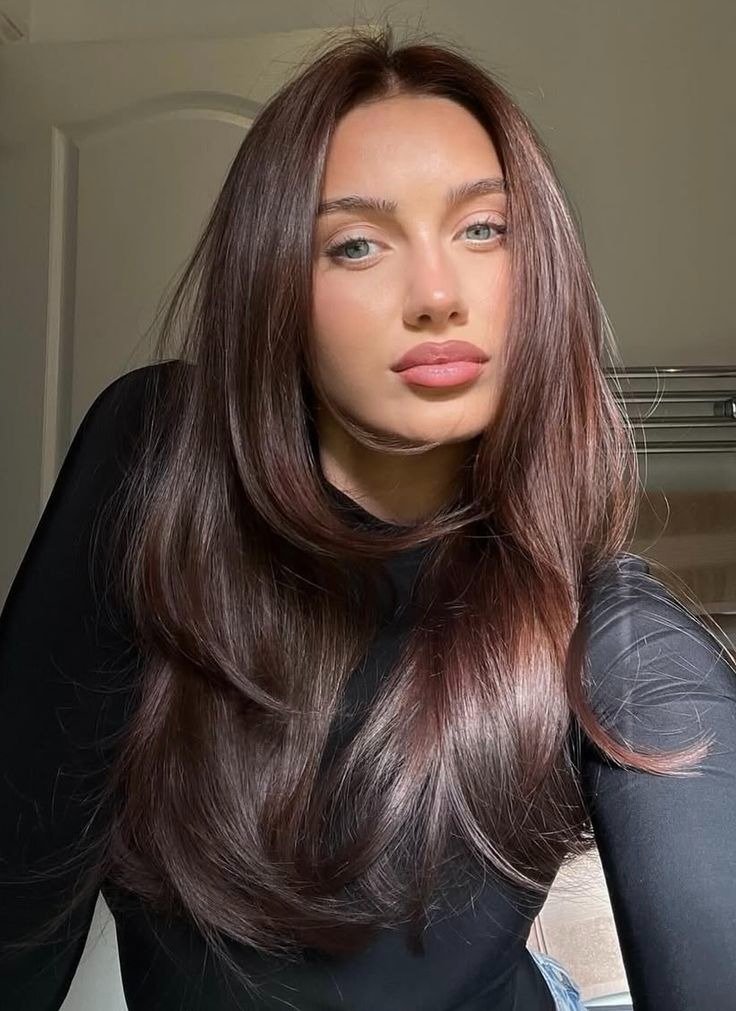 Modelo posa com blusa preta e cabelo castanho avermelhado longo e brilhante, em clima elegante e suave