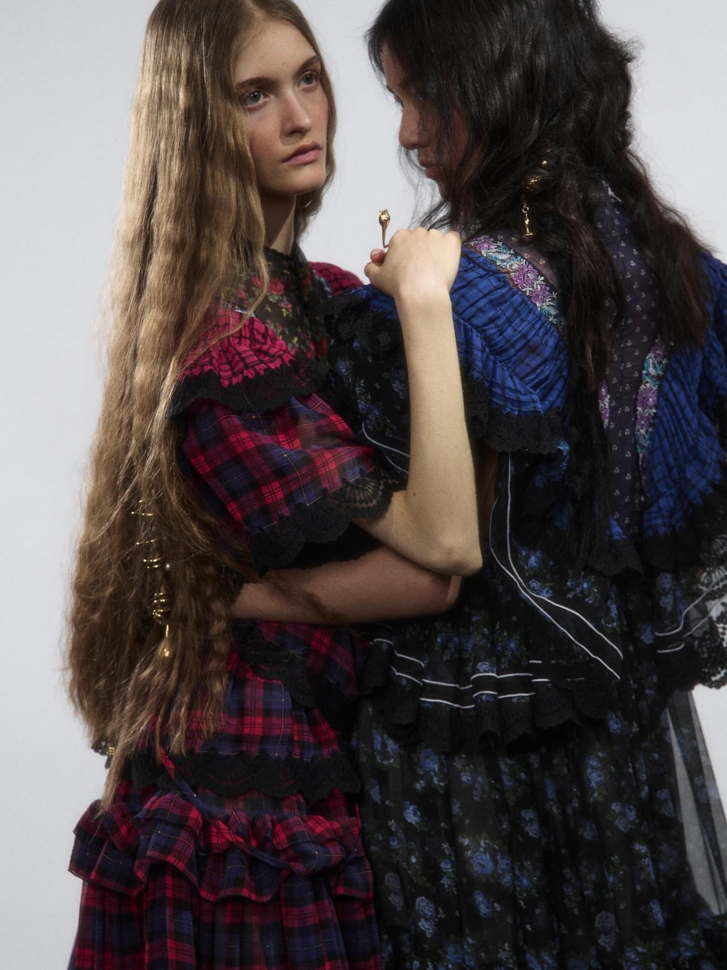 Modelos posam abraçadas com vestidos Chloé em xadrez vermelho e floral azul, com rendas e babados delicados que revelam um