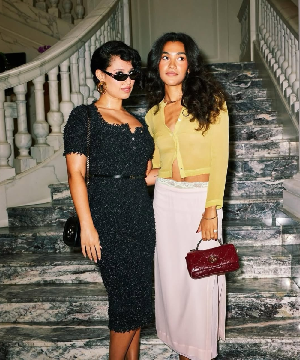 Olivia Dean e Raye posam com cabelos escovados em escadaria.