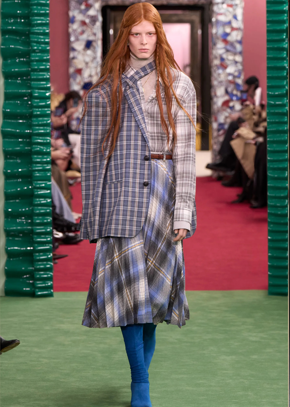 Outono/Inverno 2026: modelo posa com alfaiataria xadrez assimétrica em azul e cinza, saia fluida e clima sóbrio.