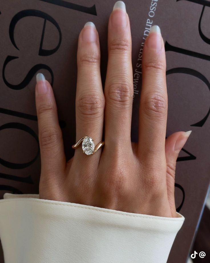 Anel de noivado com design delicado em ouro amarelo e pedra oval brilhante destaca elegância e sofisticação no dedo anelar.