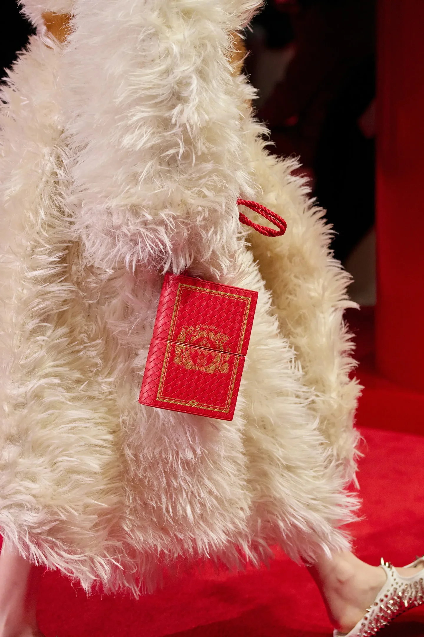 Casaco peludo branco de textura volumosa e bolsa vermelha com detalhes dourados destacam a sofisticação na temporada de