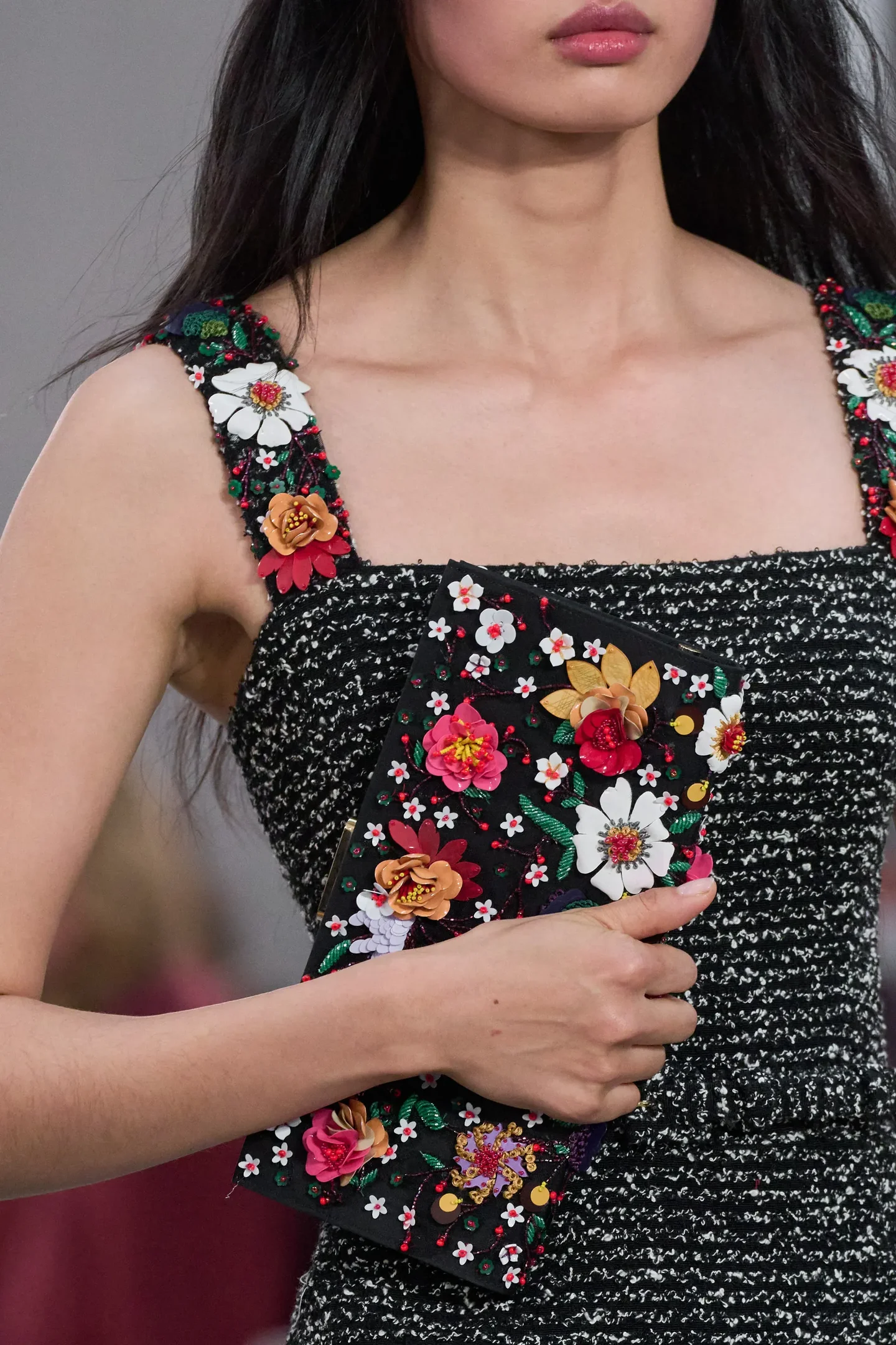 Modelo segura clutch preta com flores 3D coloridas, vestindo vestido de tweed preto e branco 