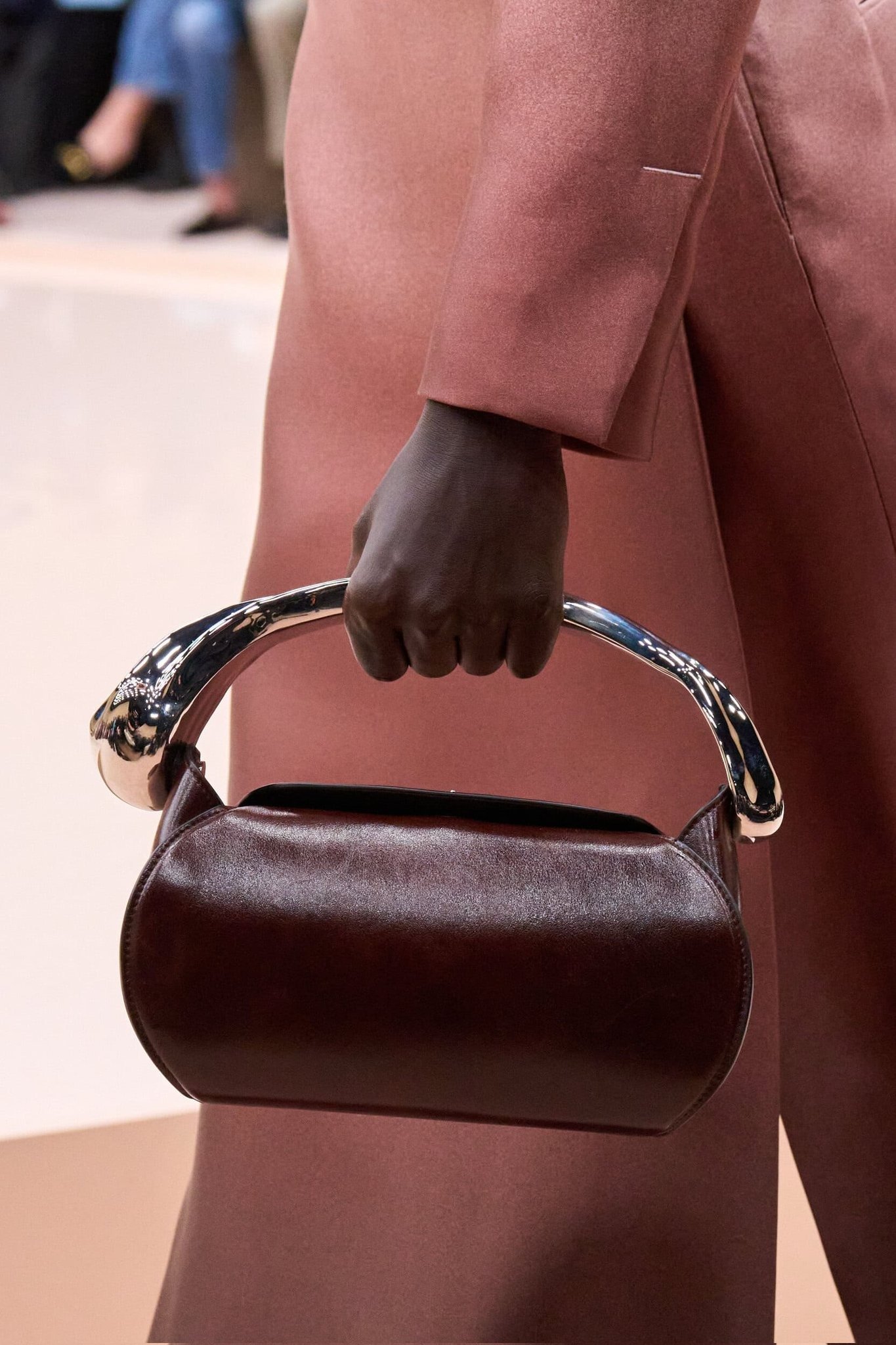 Casaco de lã rosa queimado com modelagem reta e bolsa de couro marrom com alça metálica, elegância sóbria na temporada de