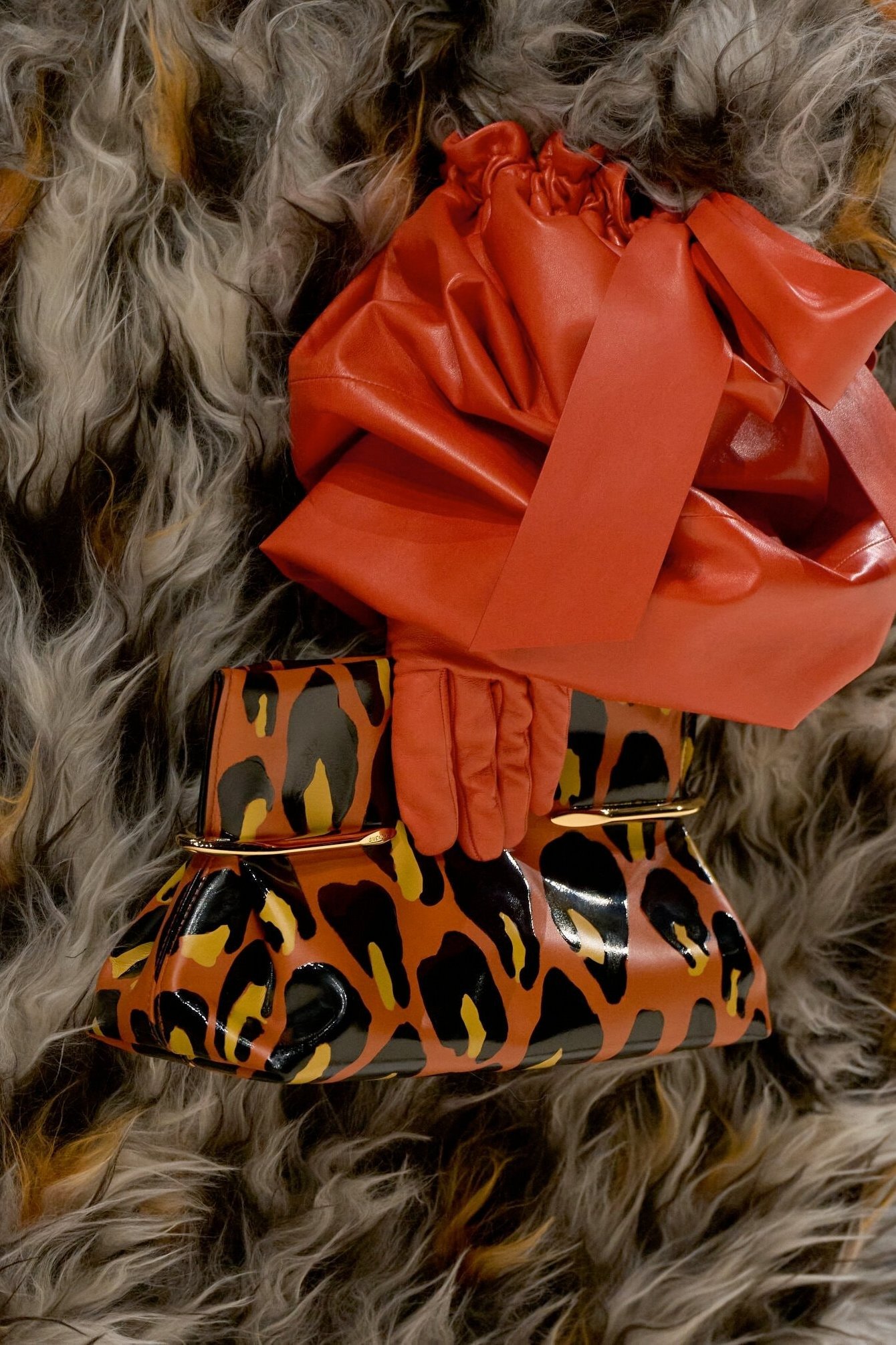 Bolsa de couro vermelho com laço, luvas combinando e clutch animal print em tons terrosos sobre pele sintética