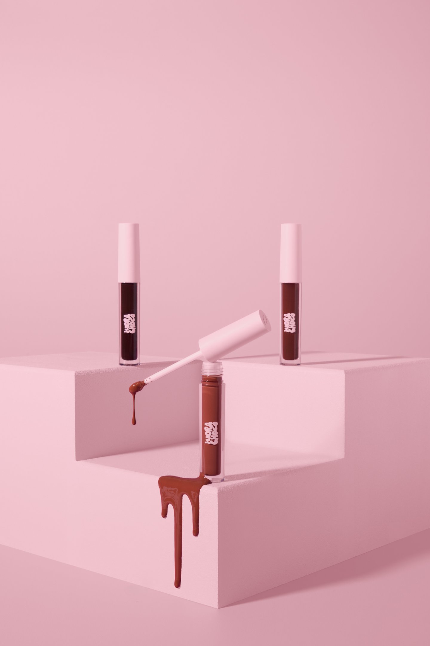 hidra choco em gloss marrom cremoso sobre cubos rosa, com aplicador aberto e efeito escorrido elegante