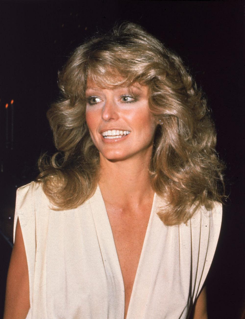 Cabelos mais icônicos das famosas ganham destaque com ondas volumosas e loiro dourado vibrante, enquanto a modelo sorri.