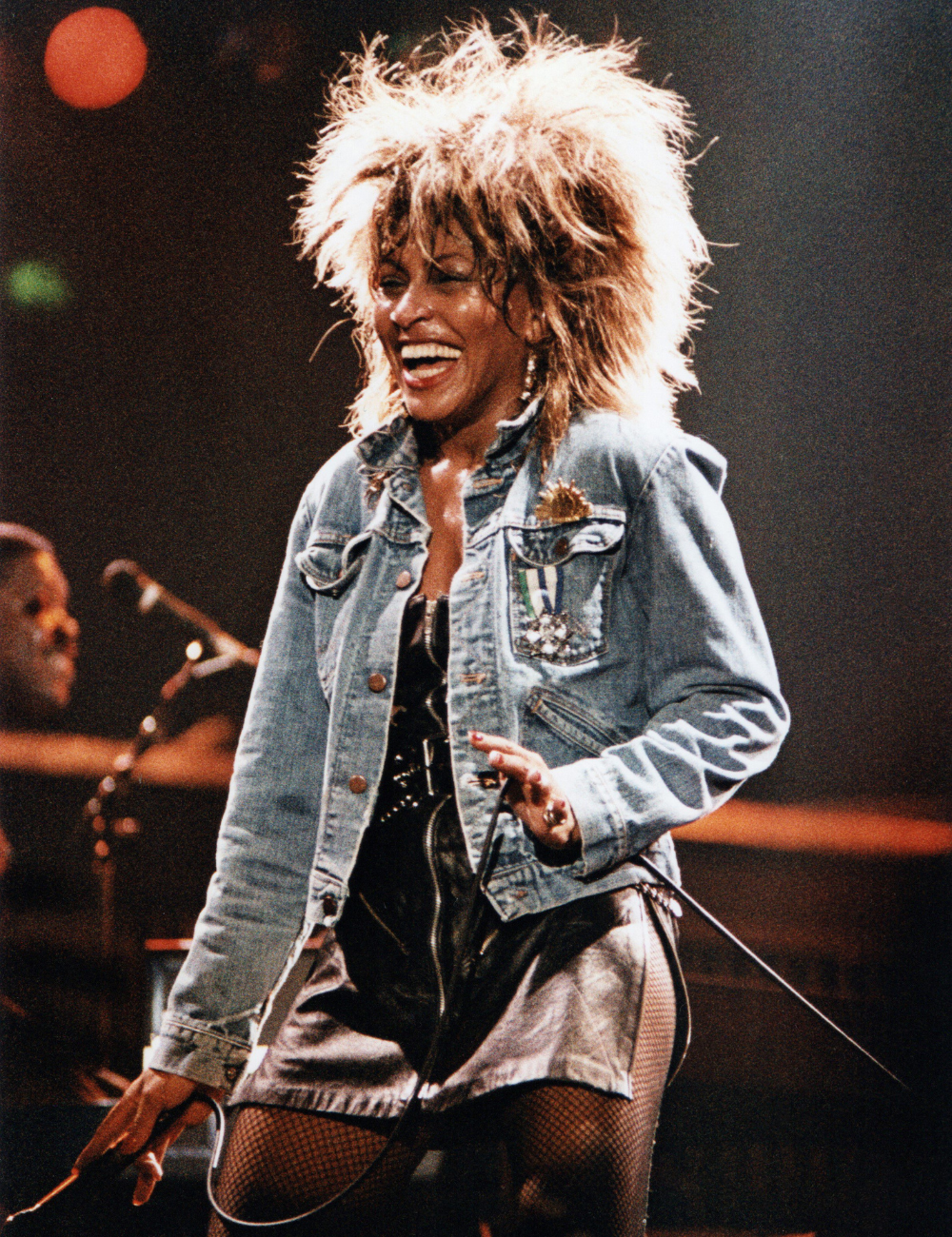 Cantora exibe cabelos mais icônicos das famosas com volume e textura marcantes, usando jaqueta jeans, saia de couro e meias.