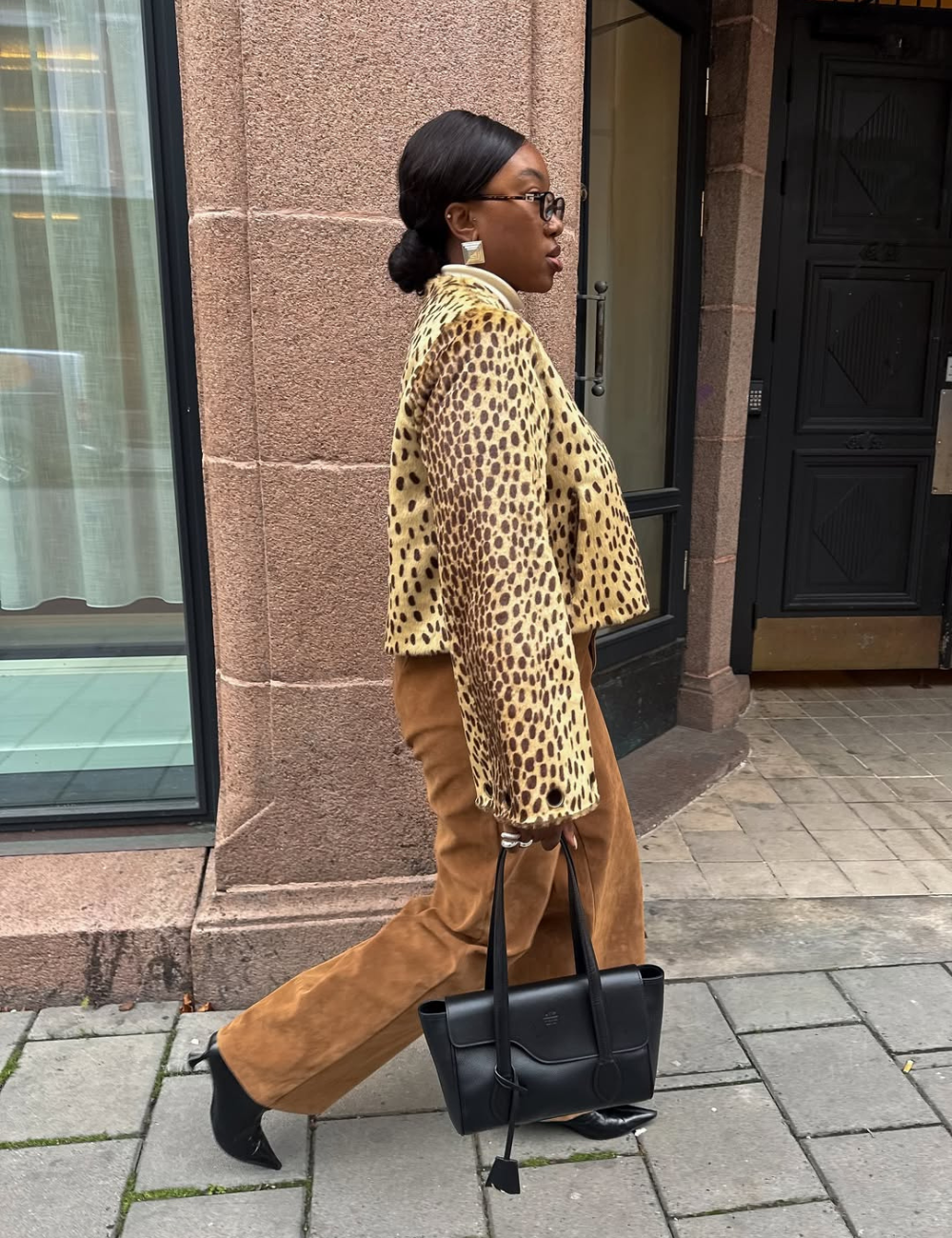 Mulher andando na rua enquanto usa casaco com estampa de animal print e calça de veludo marrom.