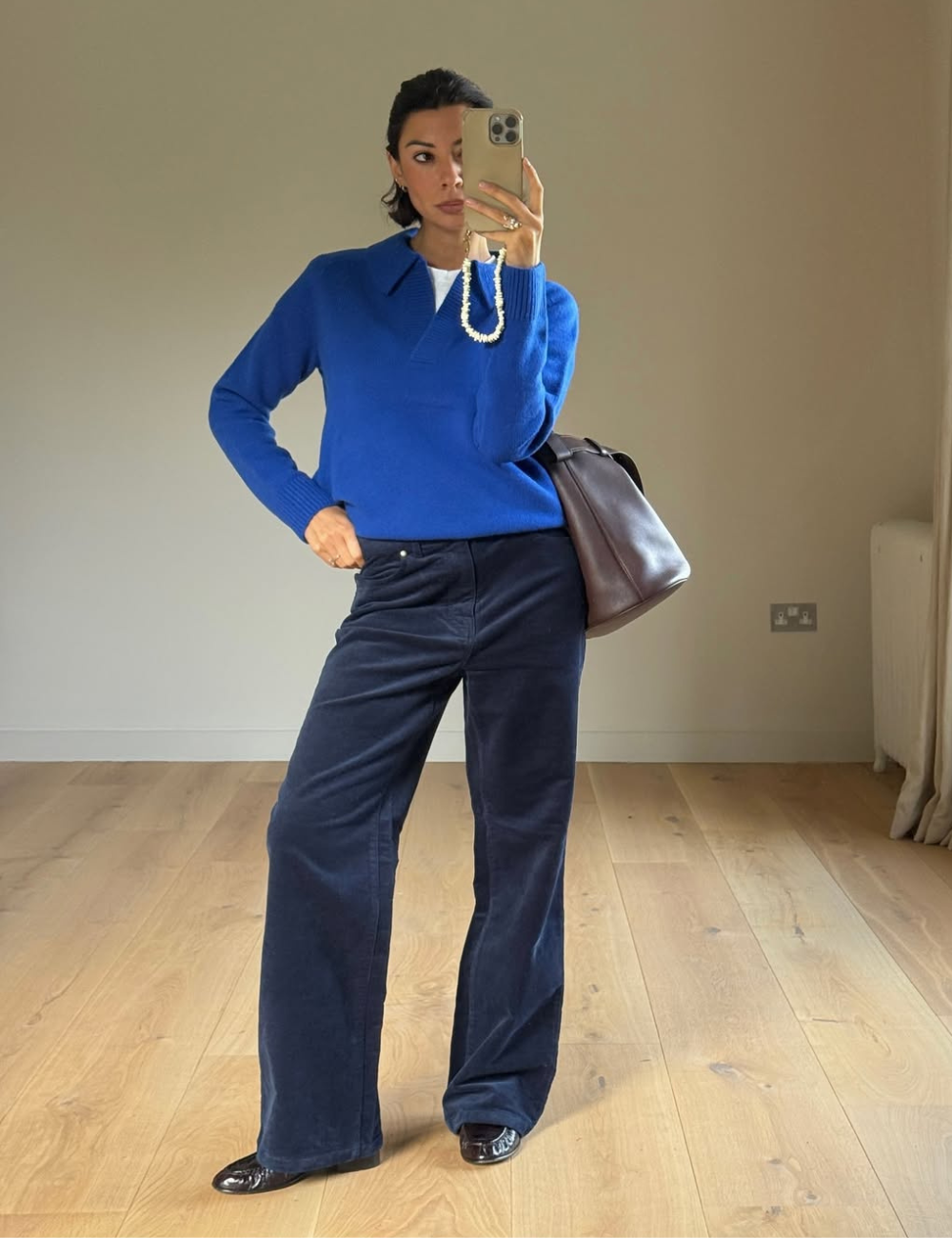 Mulher tira foto no espelho usando um suéter azul, calça de veludo também azul e sapatos pretos.