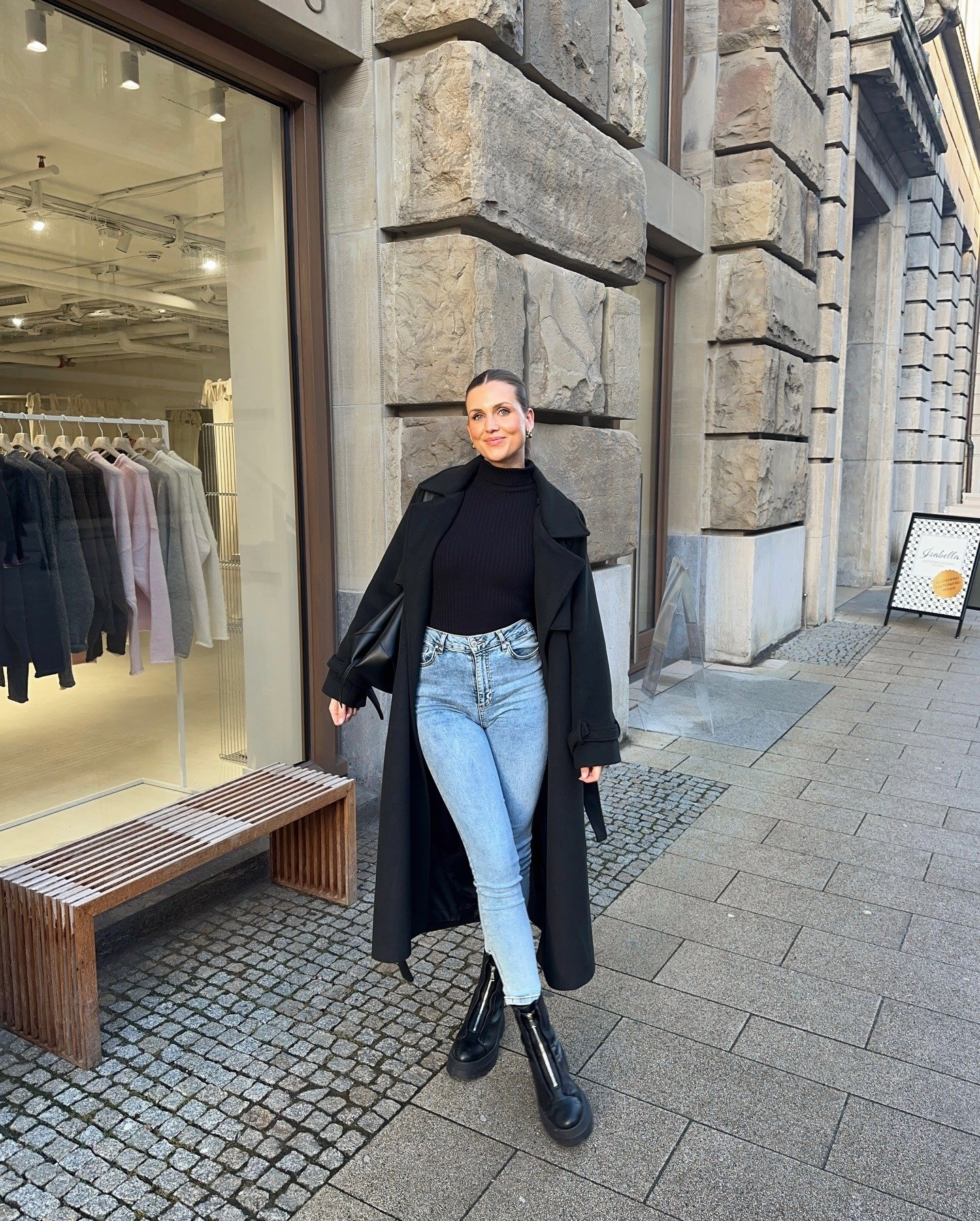 Modelo posa com calça skinny jeans azul de lavagem média, jaqueta cropped combinando e sapatos pretos, em clima urbano