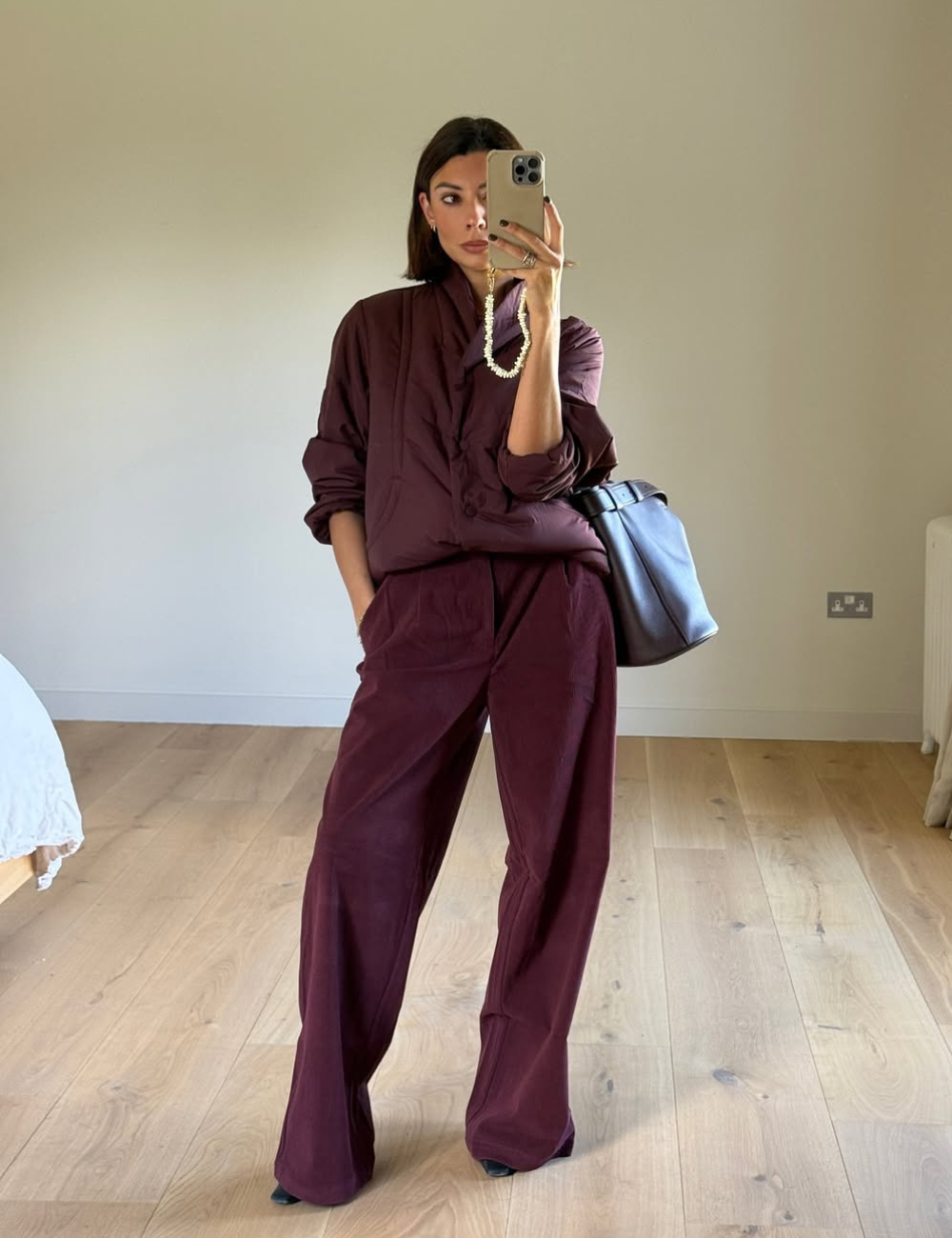 Modelo posa com calças confortáveis para trabalhar e conjunto vinho amplo, em quarto minimalista de clima elegante.