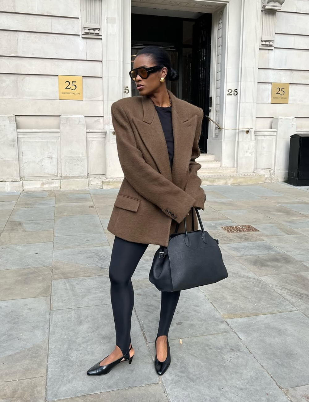 Modelo posa com blazer marrom oversized e calças confortáveis para trabalhar em preto, look elegante e urbano.