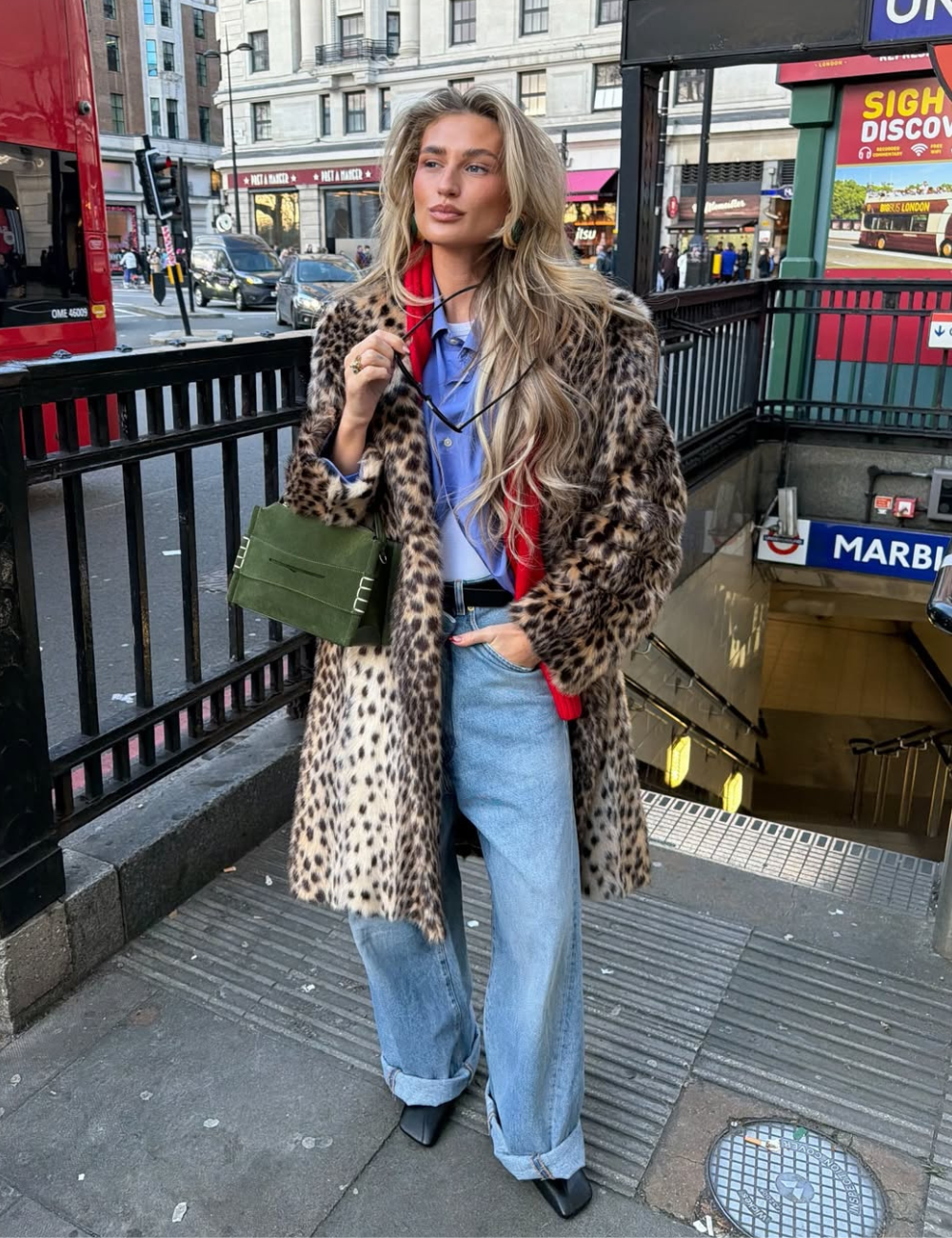 Modelo usa look maximalista com casaco feminino de oncinha, jeans baggy e bolsa verde.