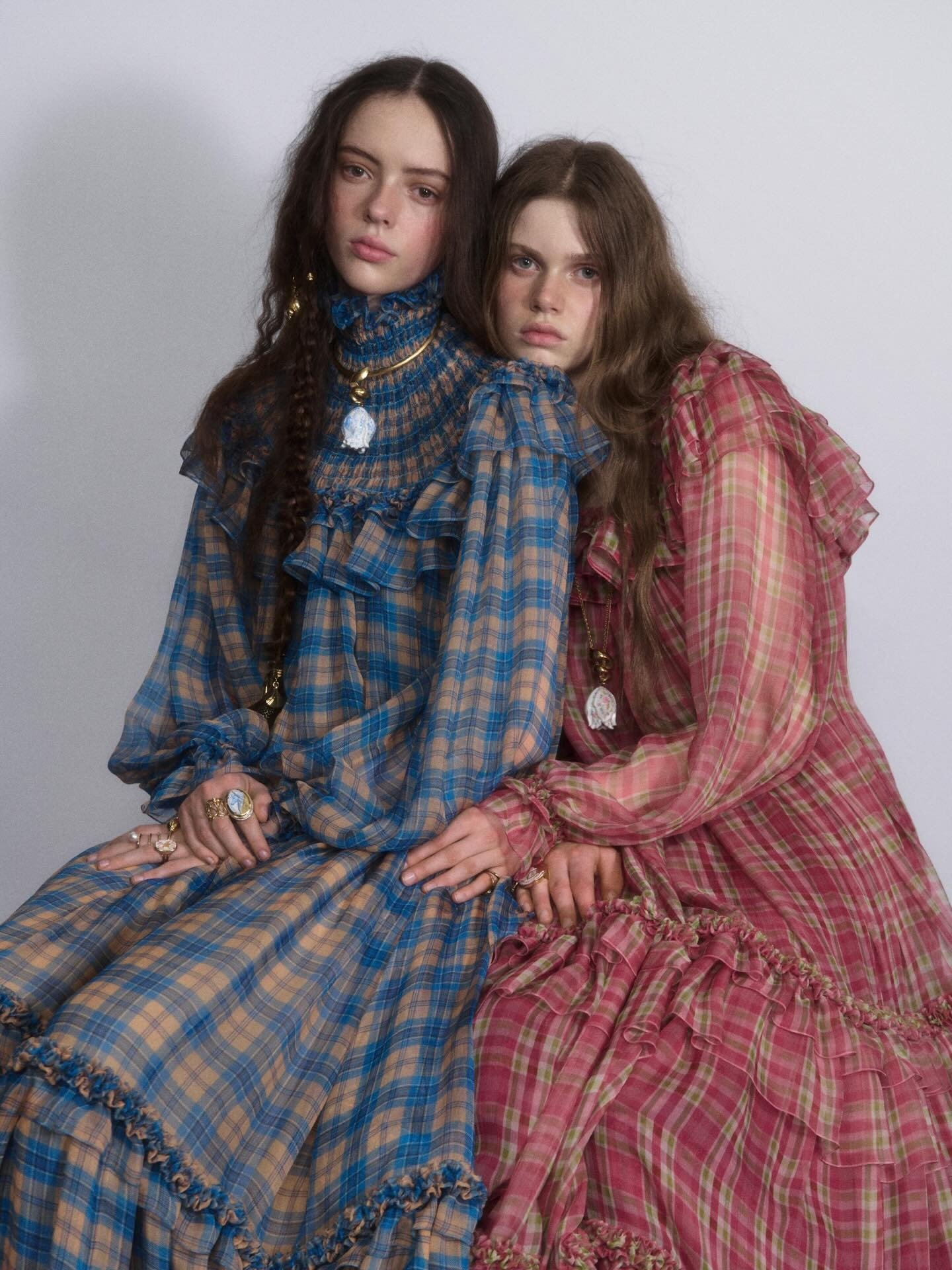 Modelos posam abraçadas com vestidos longos de Chloé em xadrez fluido, com babados e gola alta, em tons azul e rosa, clima