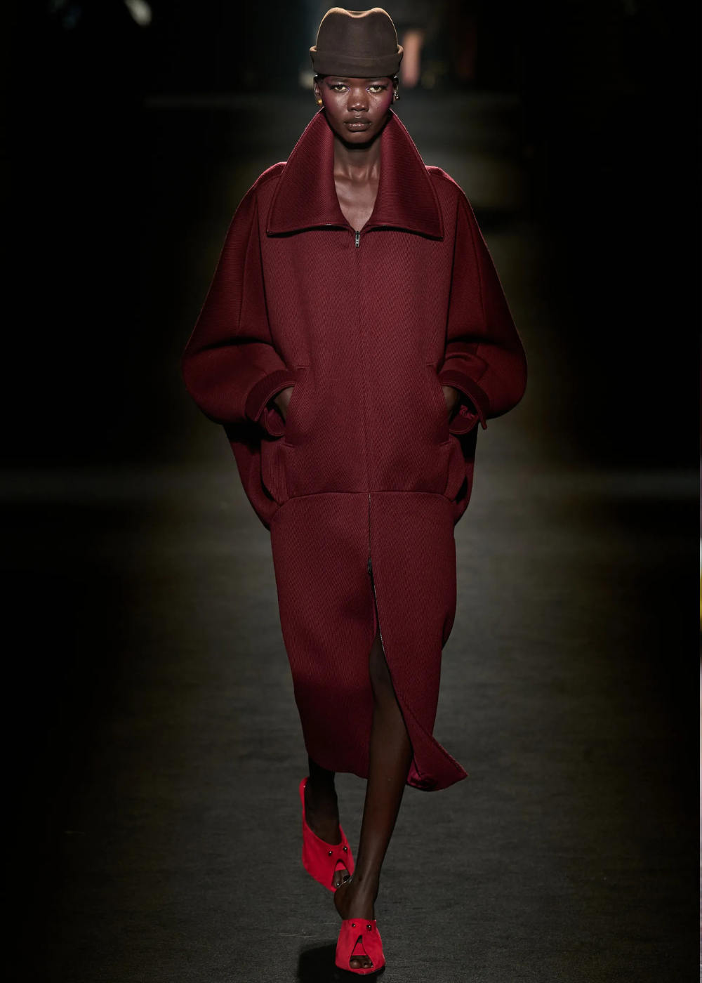 Outono/Inverno 2026: modelo posa na passarela com conjunto canelado vinho oversized, gola ampla e chapéu, em clima sóbrio.