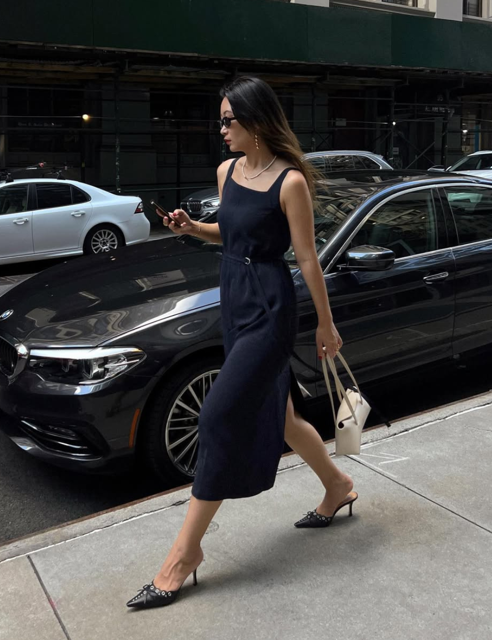 Mulher caminha confiante com vestido midi preto de alças finas e mule preta de bico fino com tachas.