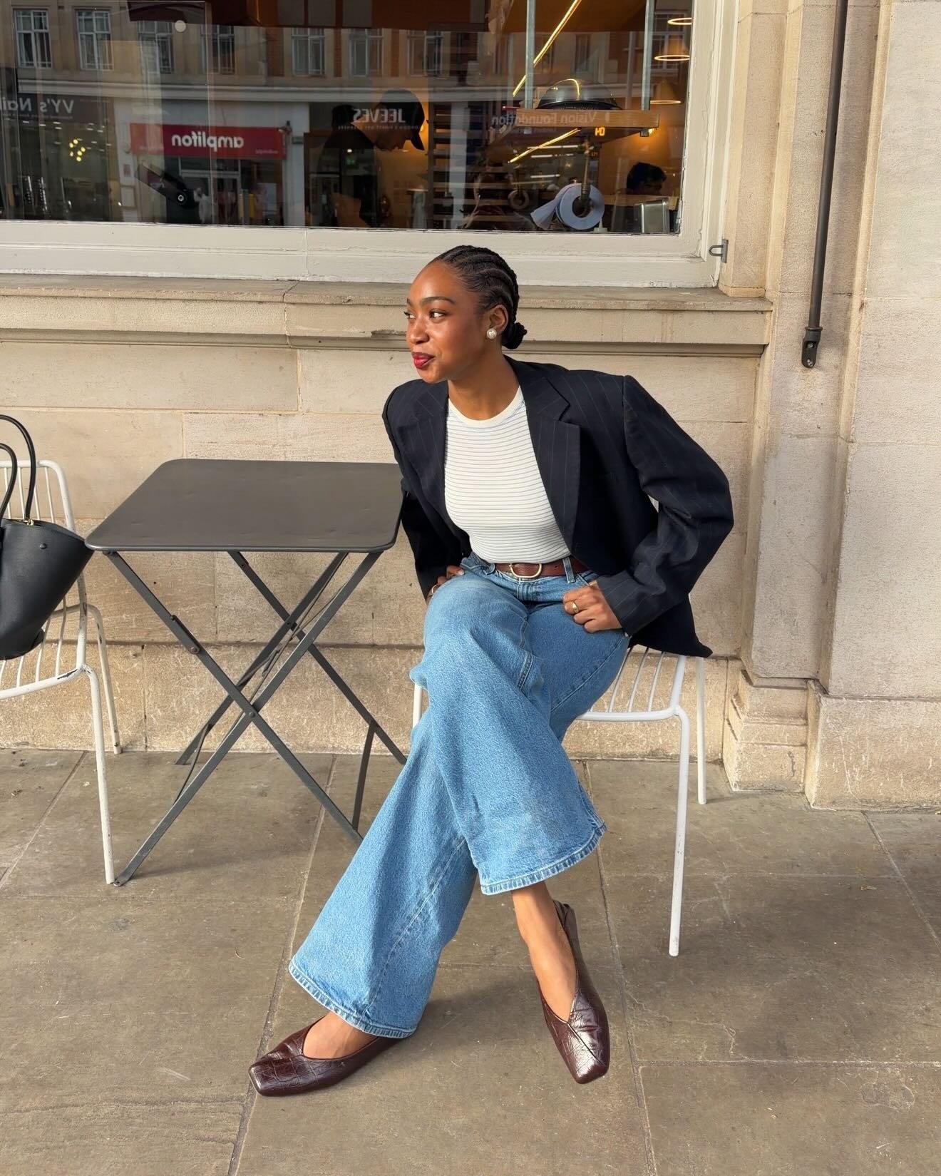 Modelo com blazer preto, malha branca, jeans amplo e sapatilha marrom, entre cores de sapato que combinam com tudo.