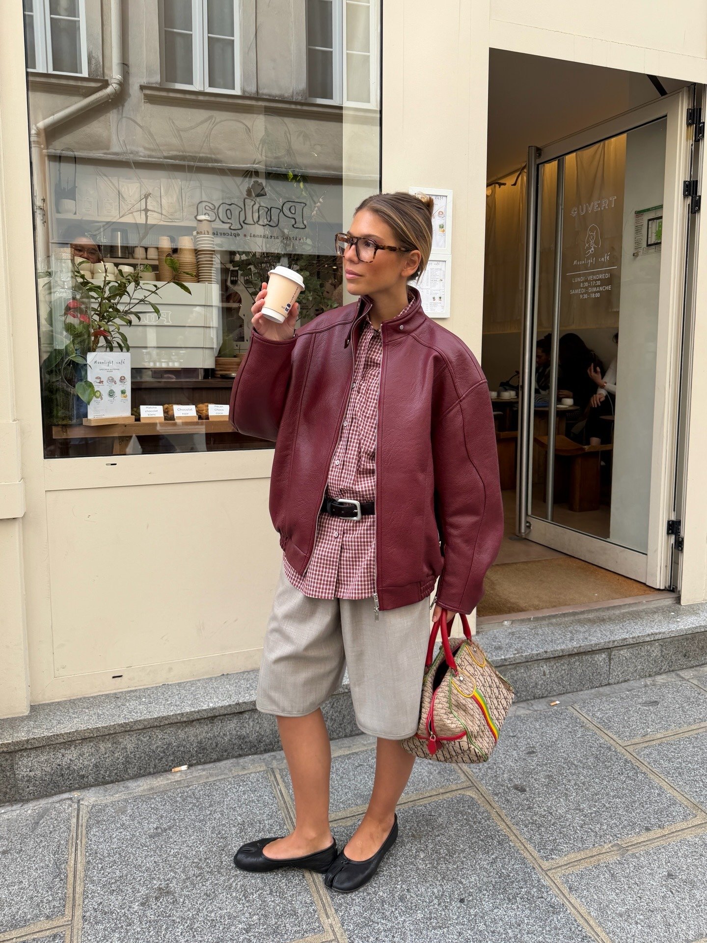 Modelo posa com jaqueta vinho e sapatilha preta, uma das cores de sapato que combinam com tudo, em clima urbano elegante.