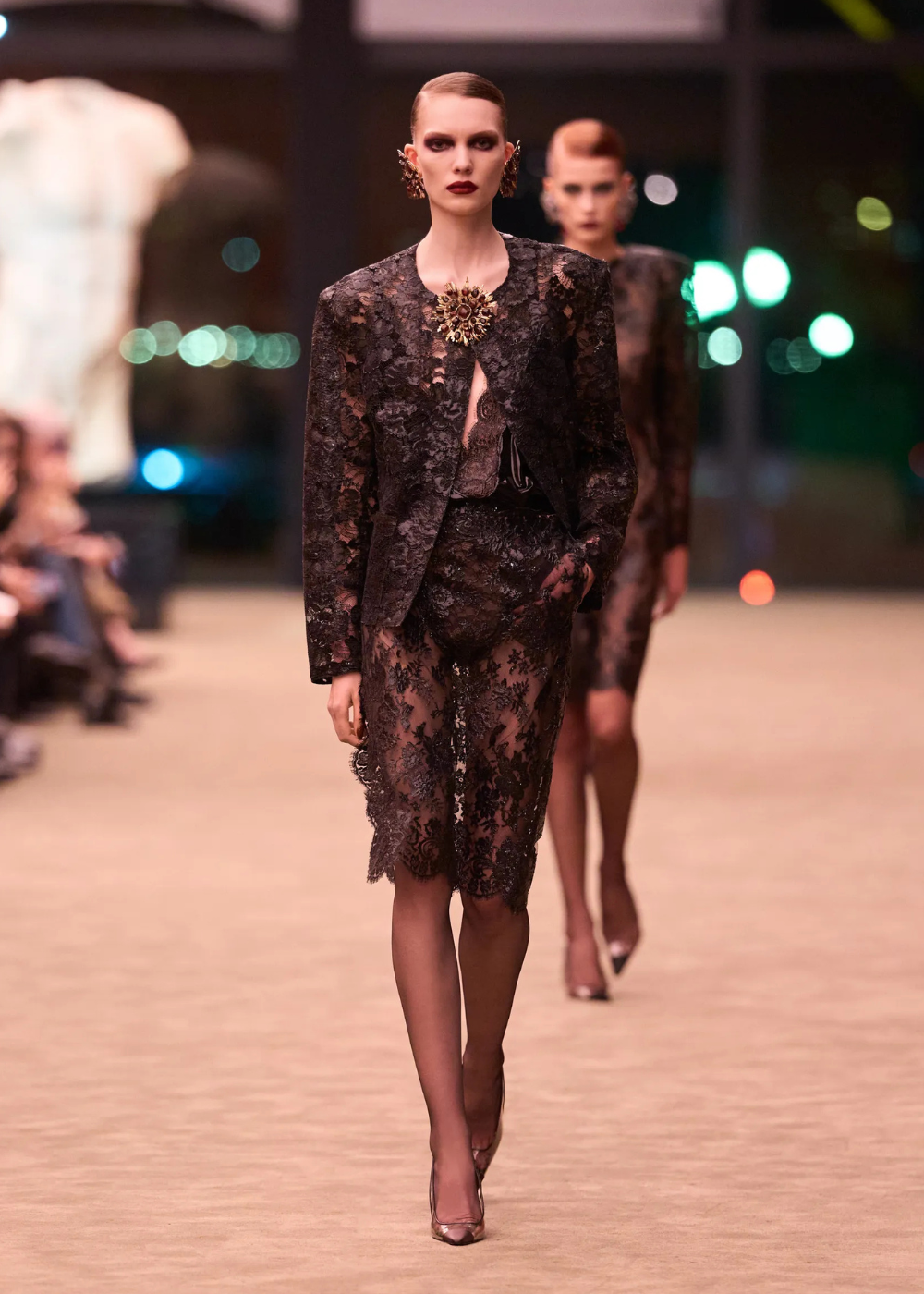 Outono/Inverno 2026: modelo desfila em renda preta com blazer estruturado, transparência e elegância sombria.