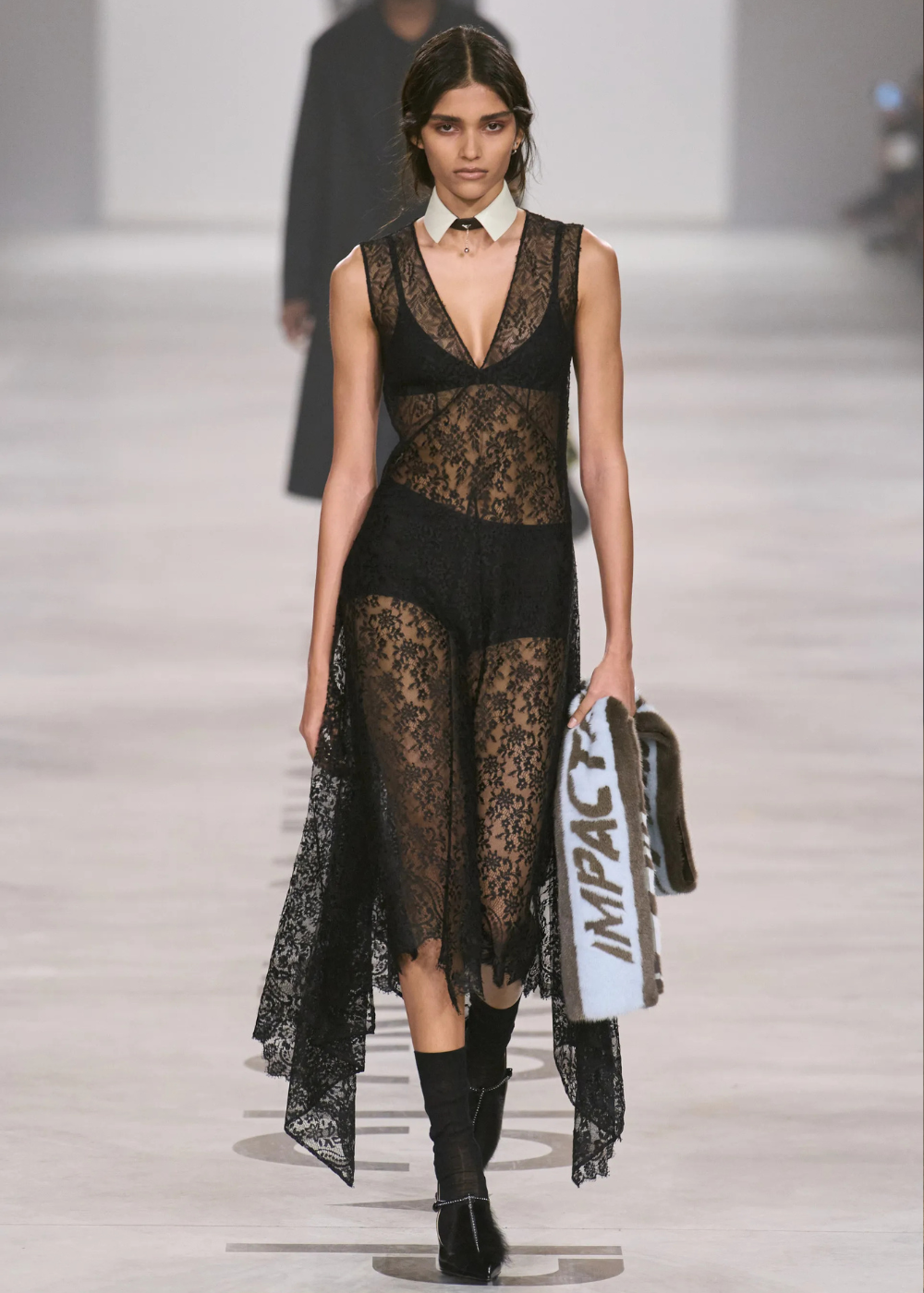 Outono/Inverno 2026: modelo desfila em renda preta transparente com gola branca e bolsa felpuda. Texto: IMPACT