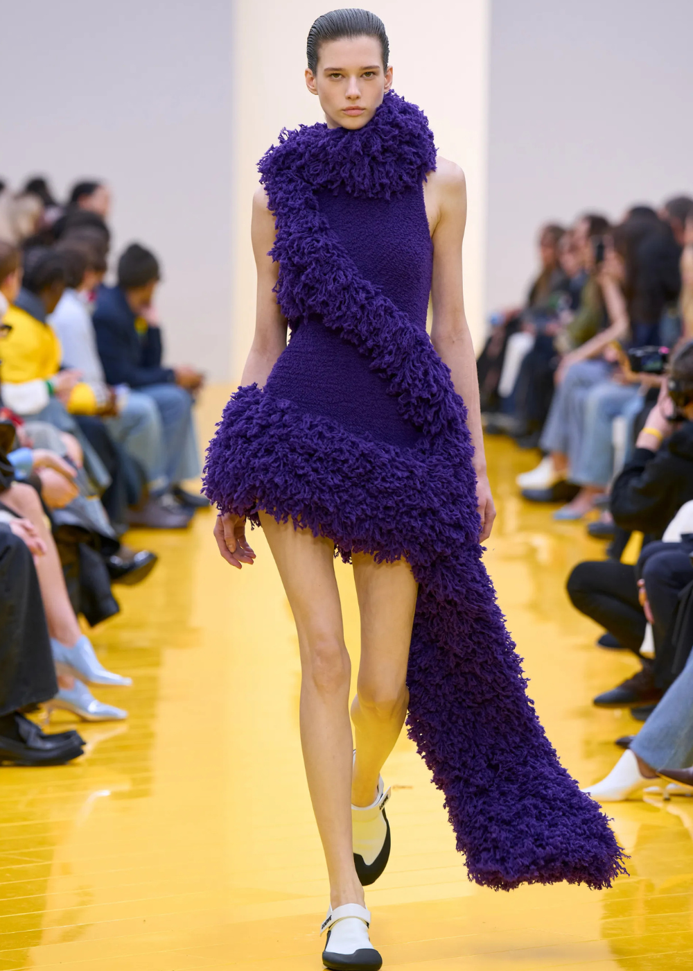 Outono/Inverno 2026: modelo desfila vestido roxo texturizado com volume felpudo e cauda longa em clima dramático.