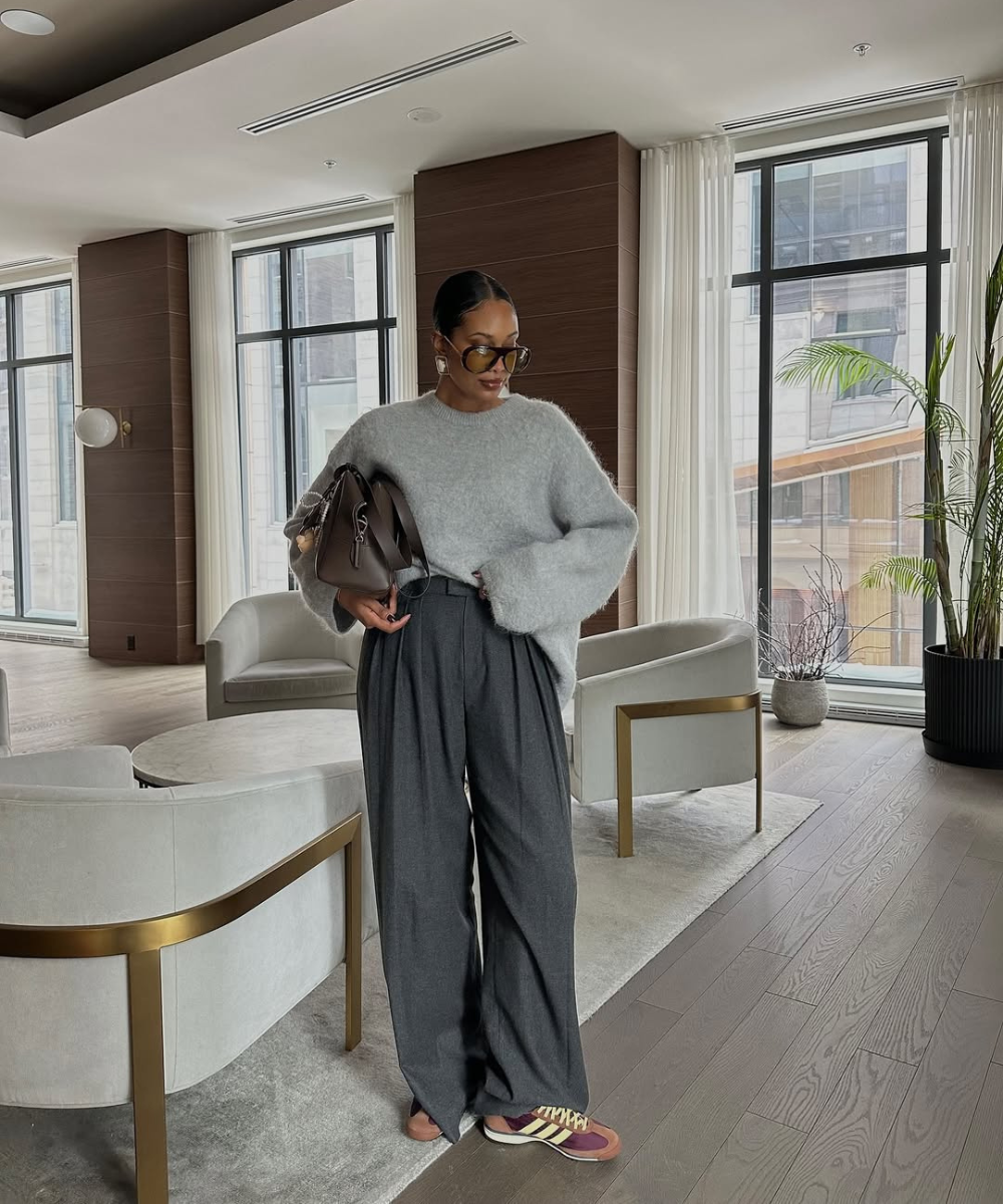 Modelo posa com calça pantalona cinza, suéter macio e tênis retrô colorido em sala elegante.