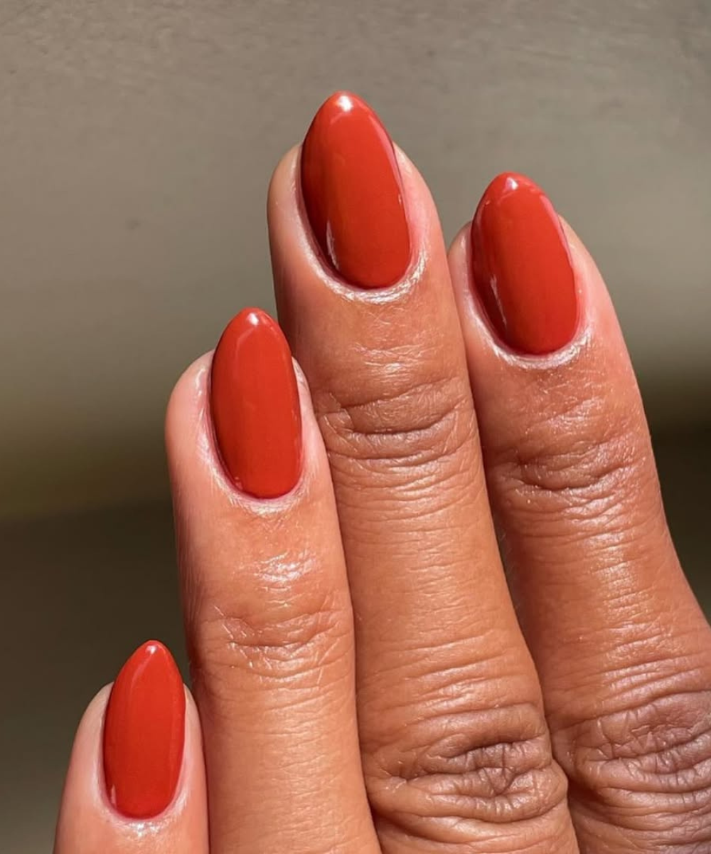 Esmaltes para o outono em unhas amendoadas terracota brilhante destacam a mão em close com elegância acolhedora