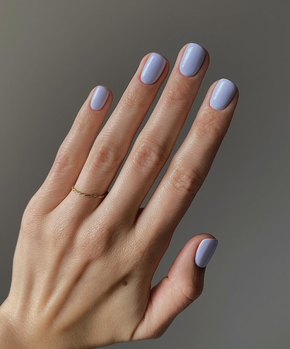 Esmaltes para o outono em tom lavanda claro com acabamento cremoso, mão posa com anel fino dourado sobre fundo cinza.