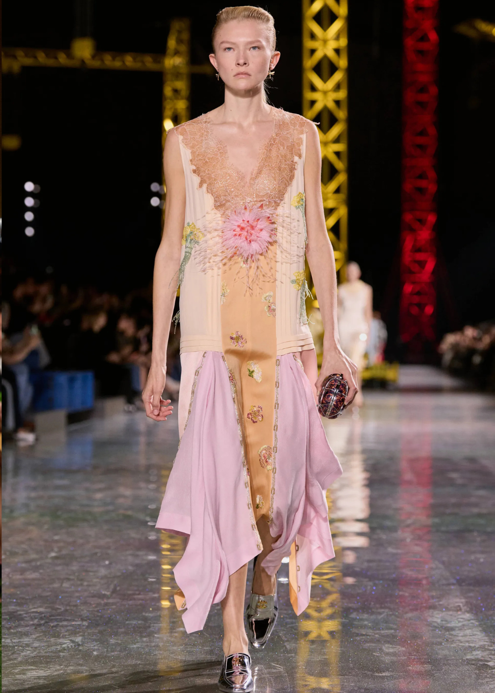 Outono/Inverno 2026: modelo desfila vestido fluido bordado em rosa e nude, renda e recortes assimétricos, clima etéreo.