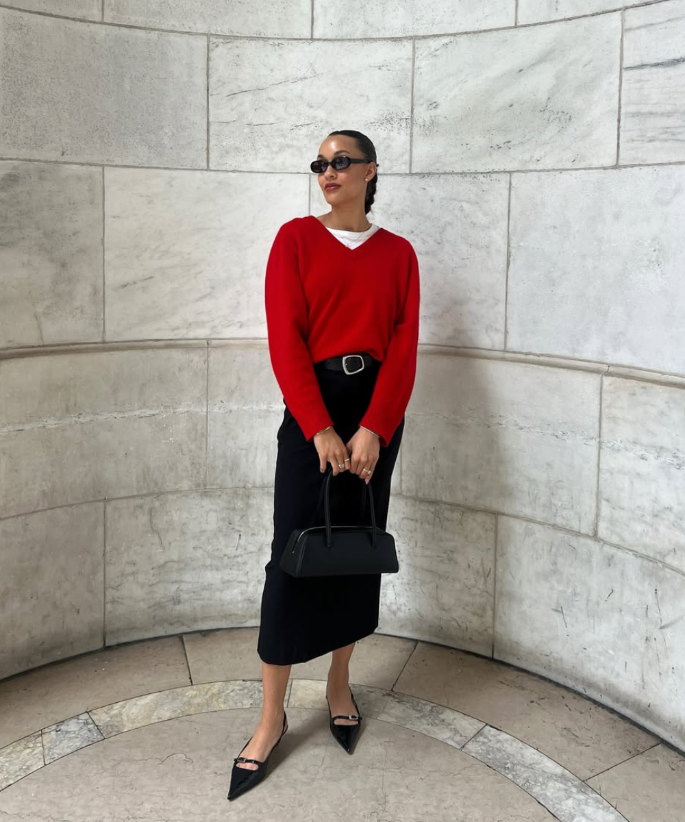 Looks com scarpin: modelo posa com tricô vermelho, saia preta midi e bolsa estruturada em cenário de pedra elegante.