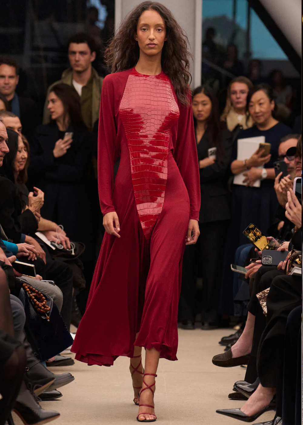 Outono/Inverno 2026: modelo posa na passarela com vestido vinho fluido e painel brilhante, em clima sofisticado.