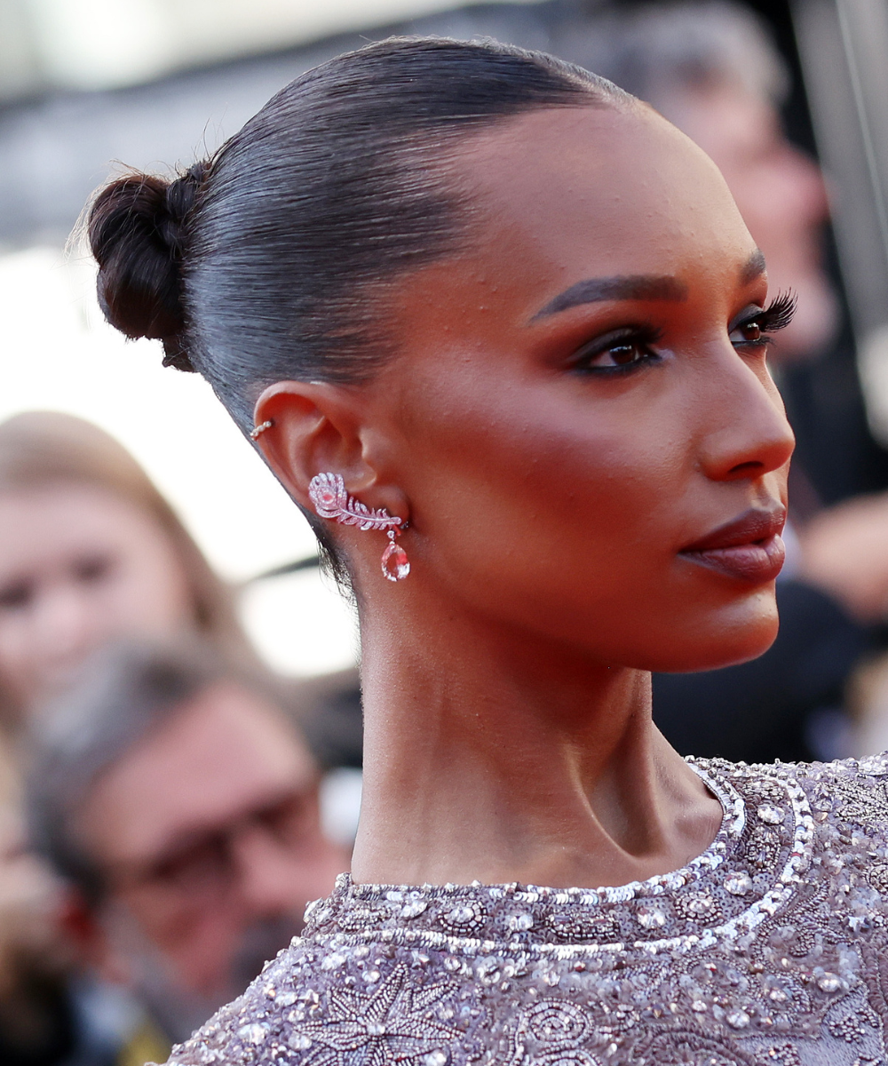 Penteados para casamento com coque polido; modelo posa de perfil com vestido bordado prateado e brinco rosa.