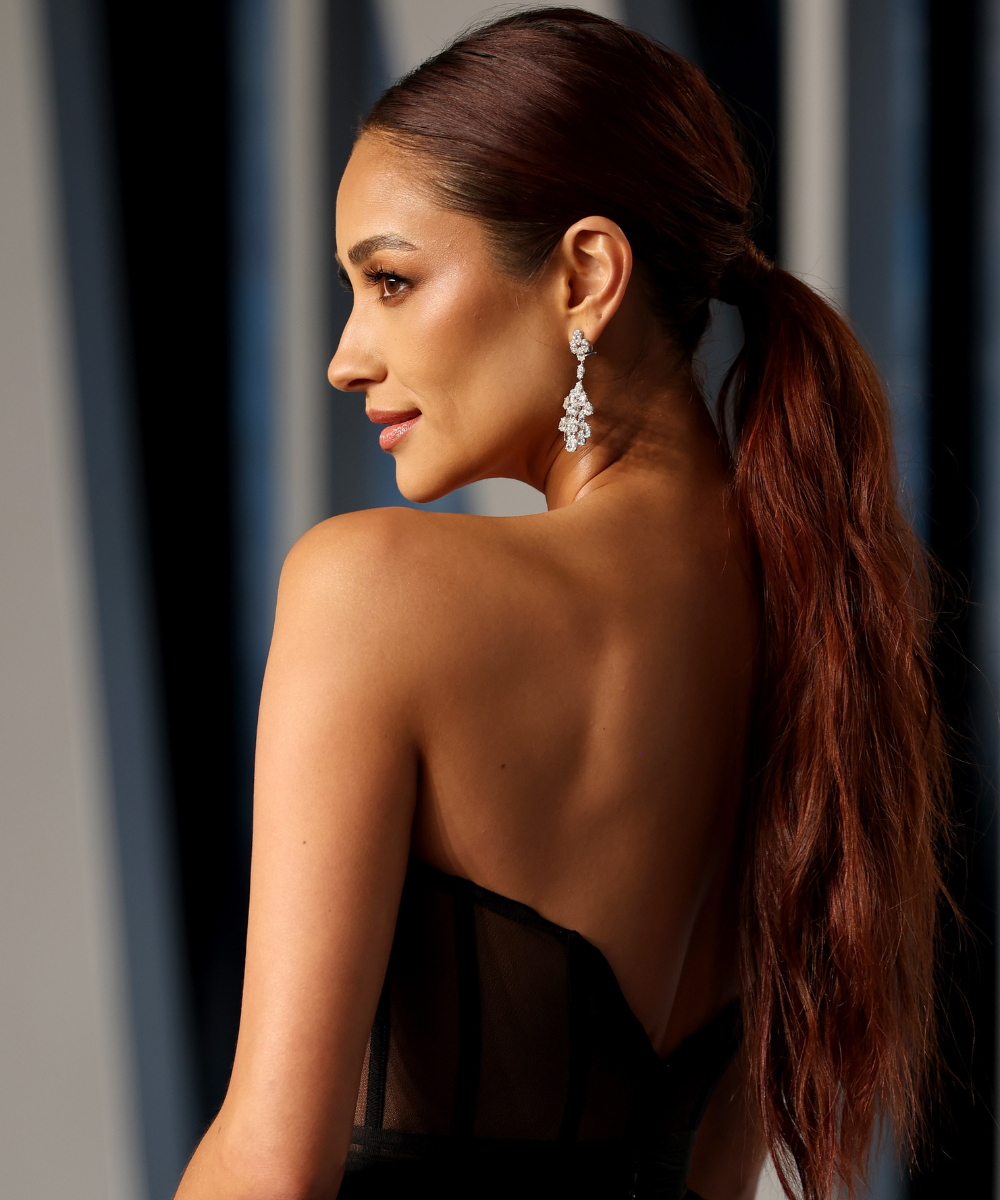 Penteados para casamento: modelo posa de perfil com rabo de cavalo polido, vestido preto sem alças e brinco brilhante.