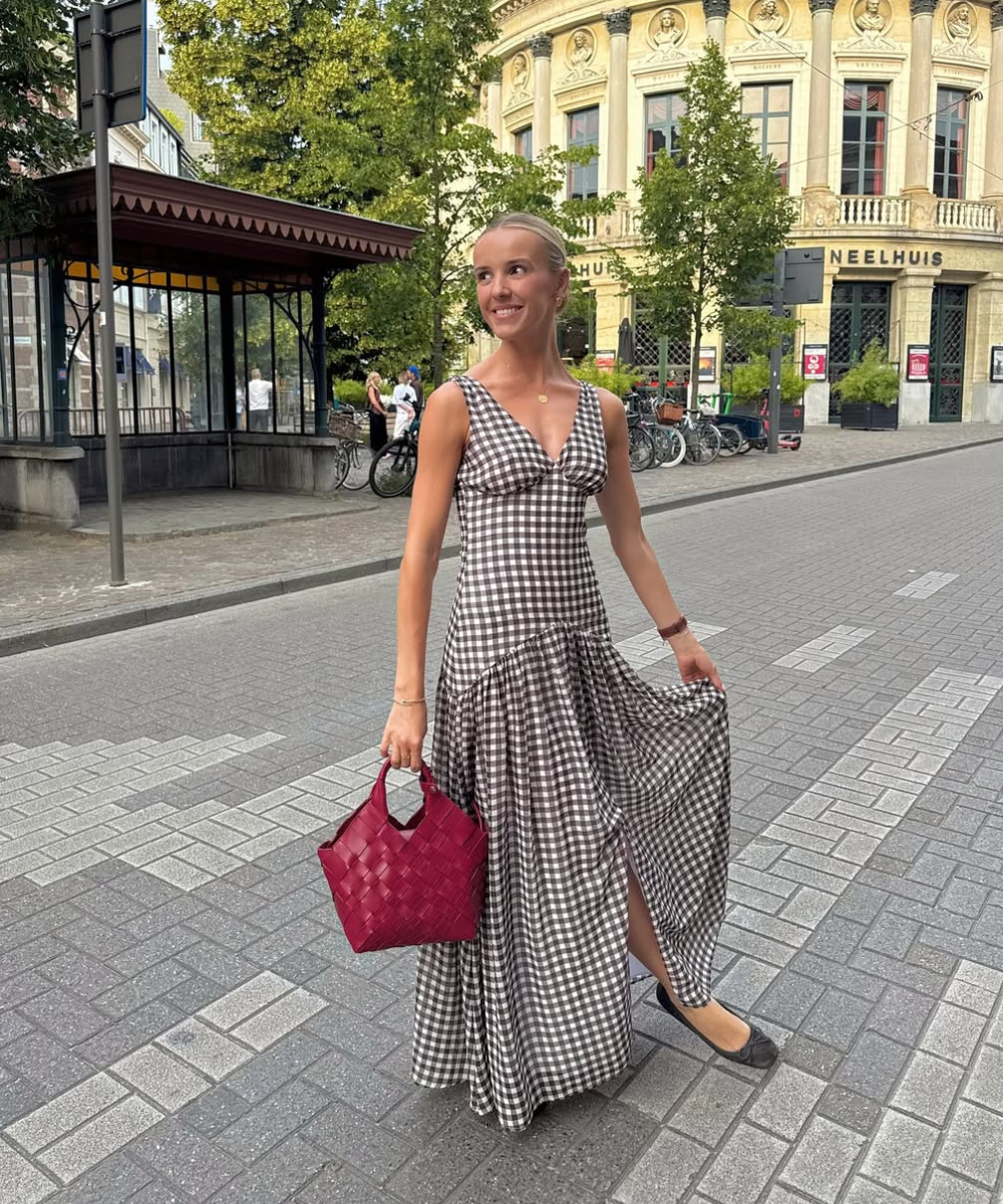 Que tipo de sapato usar com vestido soltinho: modelo posa com sapatilha preta, vestido xadrez fluido e bolsa vinho.