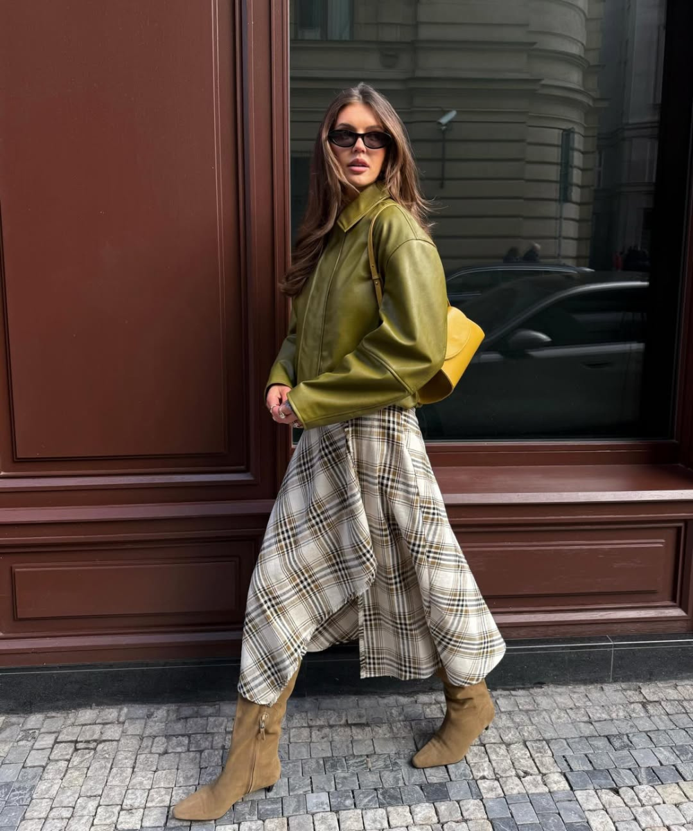 Que tipo de sapato usar com vestido soltinho: modelo posa com bota camurça bege, vestido xadrez fluido e jaqueta verde