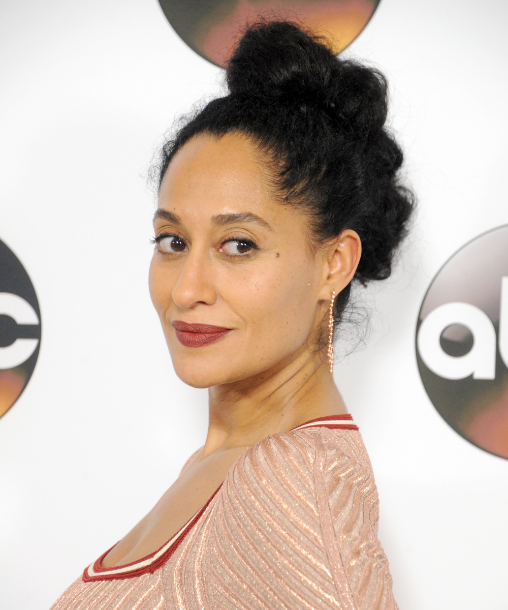 Penteados para casamento: Tracee Ellis Ross posa com coque alto texturizado, vestido rosé brilhante e elegância suave.