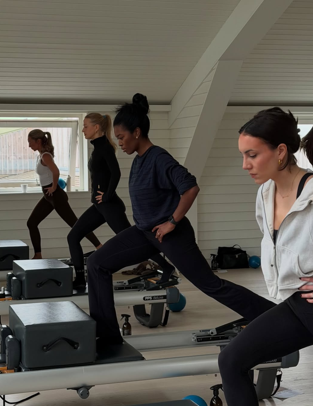 Como ter mais disposição para treinar: mulheres alongam em looks fitness preto e branco, clima focado em estúdio claro.