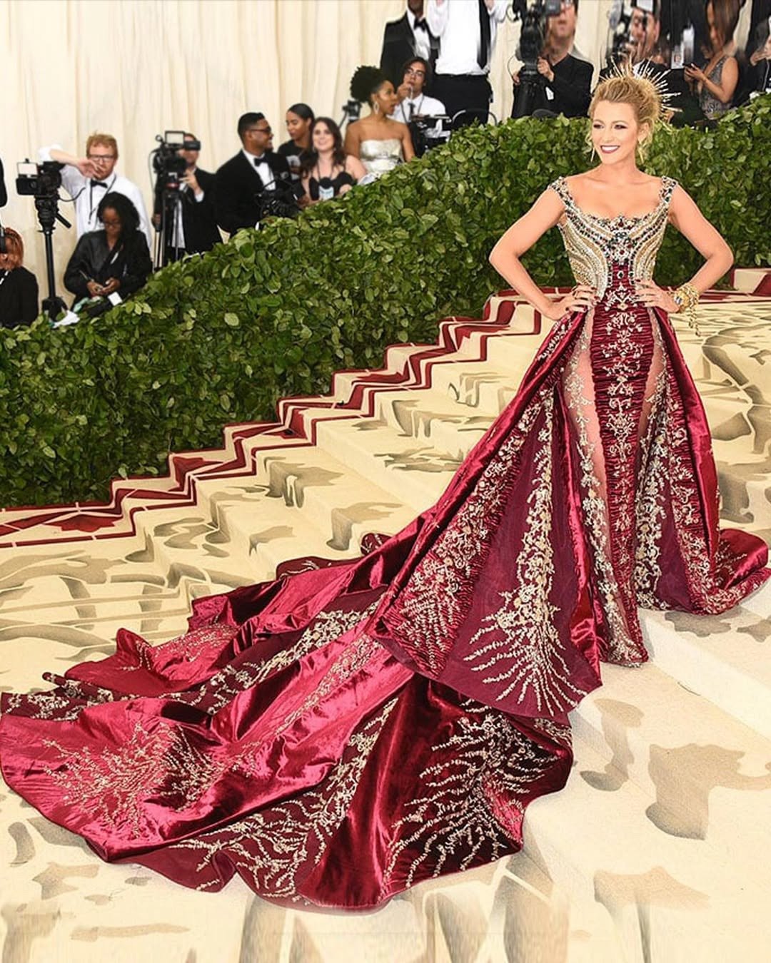 Modelo posa com vestido Versace bordado em veludo vinho e detalhes dourados, cauda longa e estrutura marcada, exalando